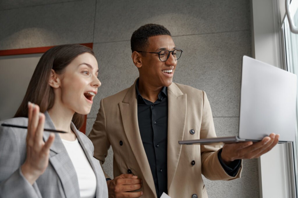 Two surprised business people working with laptop together standing near window - Home Builder Marketers